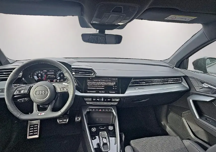 Vue intérieure avant de l'Audi A3 Sportback 2026, tableau de bord noir avec volant sport multifonction et écran central tactile.