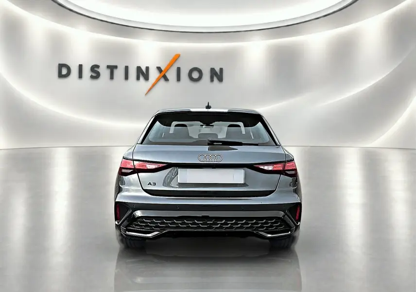 Vue arrière d'une Audi A3 Sportback gris Daytona 2026 avec feux LED et diffuseur noir dans un showroom lumineux.