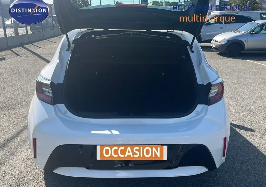 Vue arrière d'une Toyota Corolla blanche 2023 avec coffre ouvert sur un parking ensoleillé.