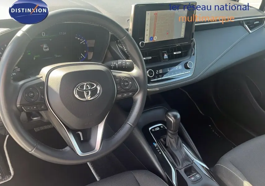 Intérieur de la Toyota Corolla 2023 hybride, vue du poste de conduite avec volant multifonction et écran tactile central.