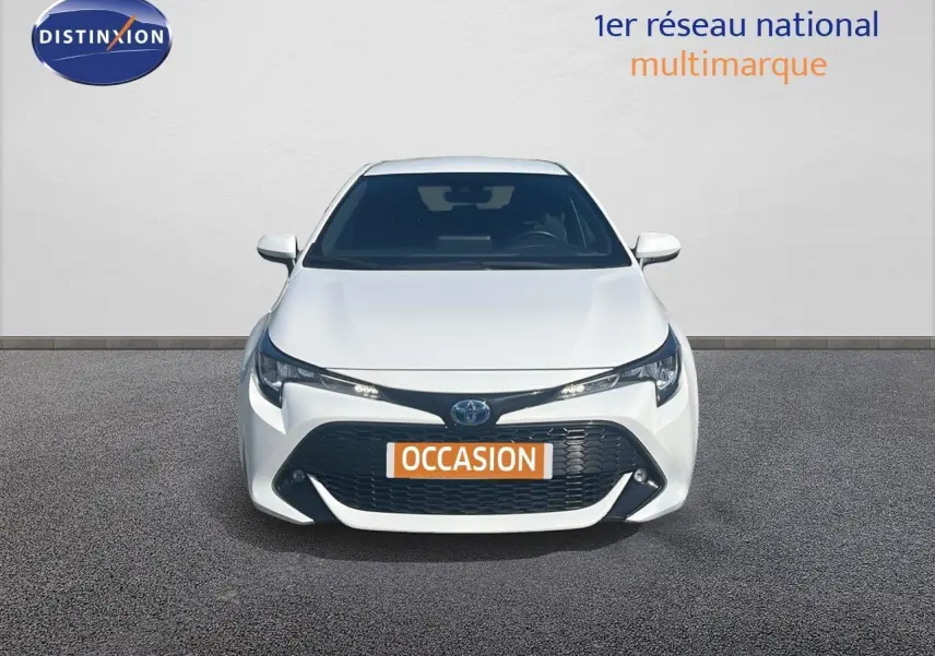 Vue frontale d'une Toyota Corolla 1.8 HSD blanche avec calandre noire et plaque "OCCASION" visible.