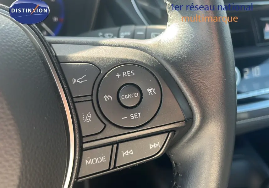 Gros plan sur les commandes au volant d'une Toyota Corolla blanche hybride 2023, mettant en valeur les boutons de régulateur de vitesse.