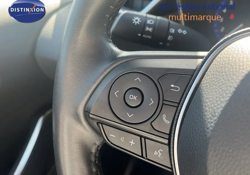 Gros plan sur les commandes au volant noir de la Toyota Corolla blanche hybride 2023, côté gauche du conducteur.