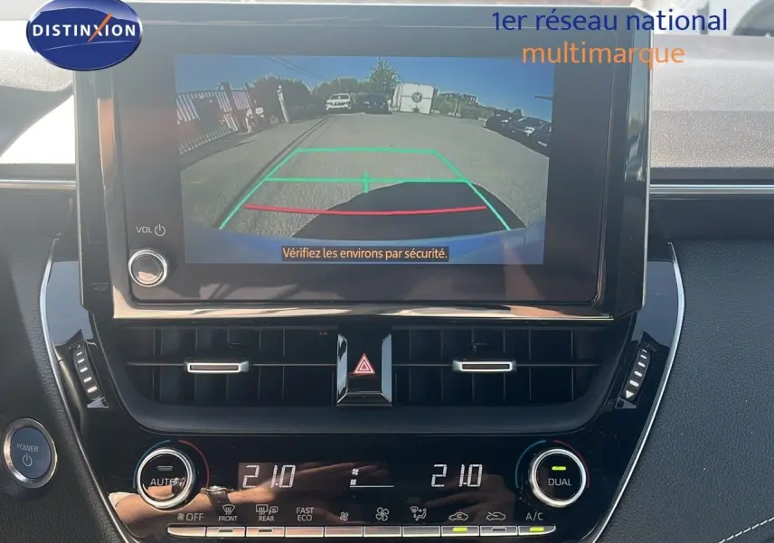 Vue rapprochée de l'écran multimédia et de la console centrale de la Toyota Corolla blanche avec caméra de recul affichée.