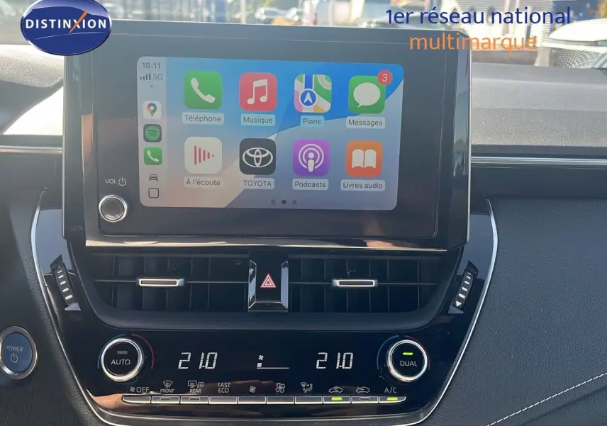 Écran tactile central affichant des applications, tableau de bord noir avec commandes climatisation sur Toyota Corolla hybride 2023.