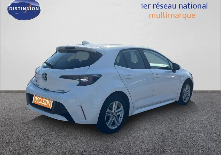 Toyota Corolla hybride blanche vue en 3/4 arrière côté droit, avec hayon et feux arrière modernes visibles.
