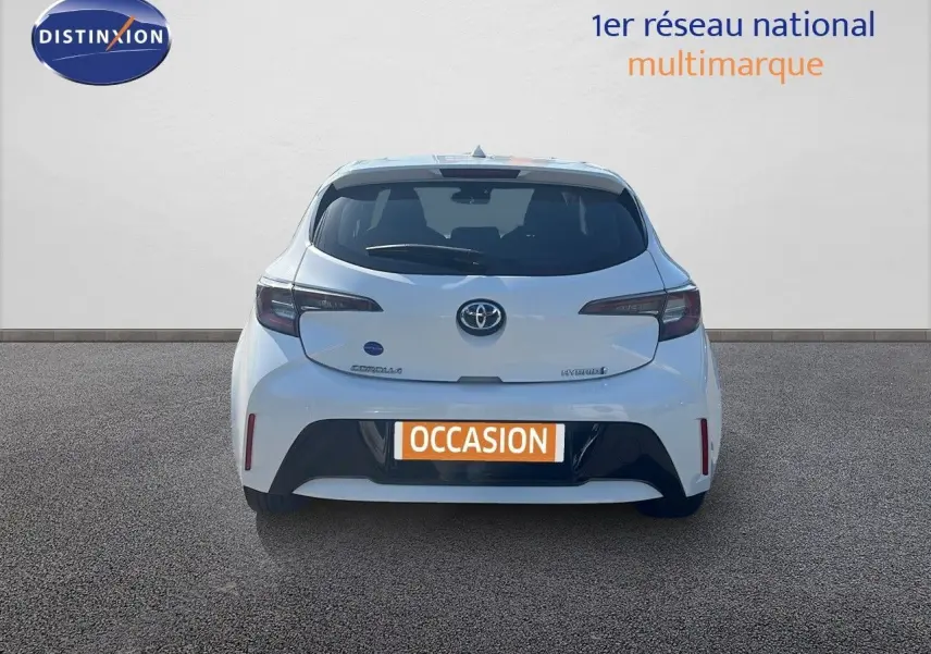 Vue arrière d'une Toyota Corolla blanche pure 2023 hybride avec plaque "OCCASION" sur fond neutre.