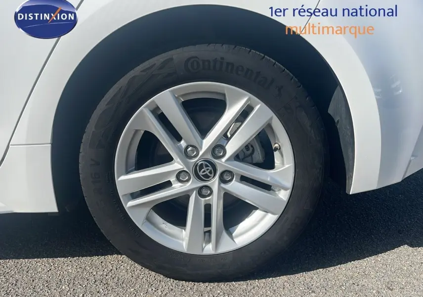 Gros plan sur la roue avant gauche blanche d'une Toyota Corolla 1.8 HSD 122CH CVT Dynamic 2023 avec jante alliage argentée.