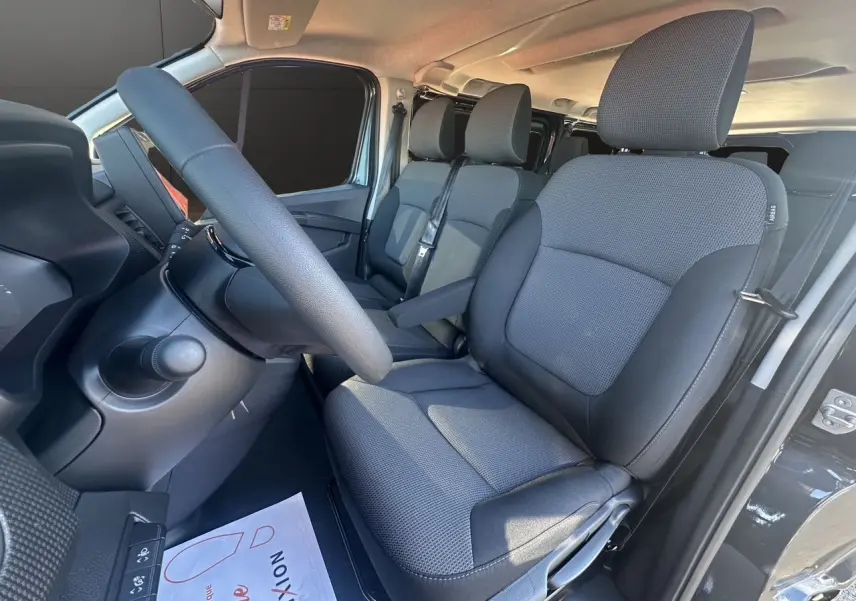 Intérieur avant droit du Renault Trafic Combi gris comète, montrant les sièges tissu noir et le volant.