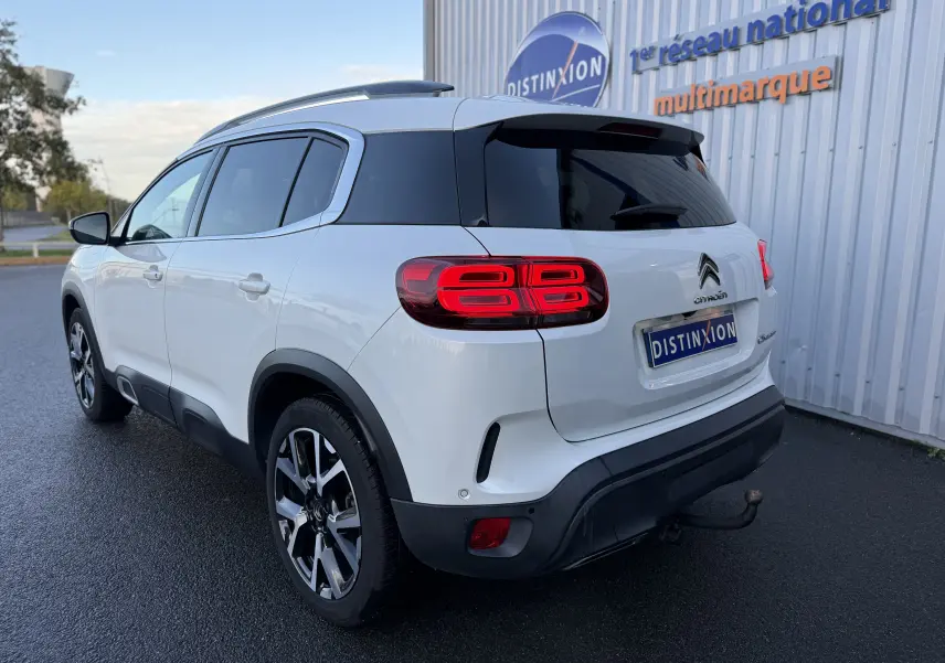 Vue 3/4 arrière droite d'un Citroën C5 Aircross blanc nacré avec feux arrière allumés et attelage visible.