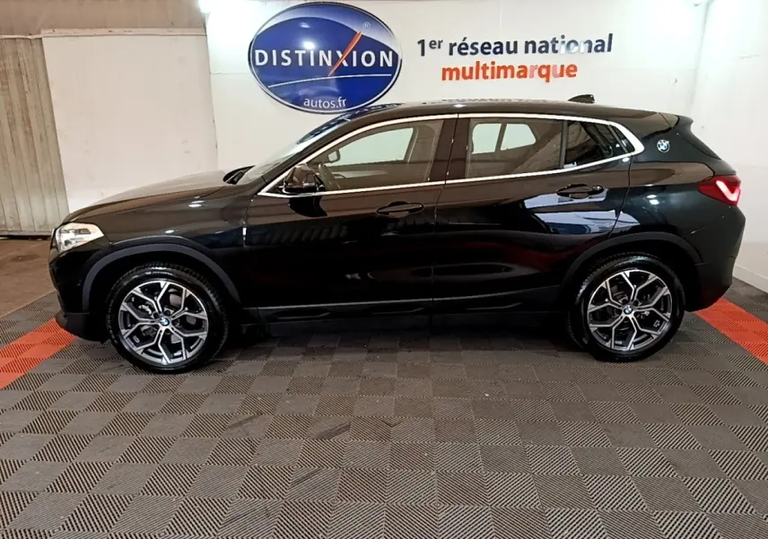 Profil droit d’un BMW X2 sDrive18i Lounge noir 2023, avec jantes alliage et feux arrière LED visibles en intérieur showroom.
