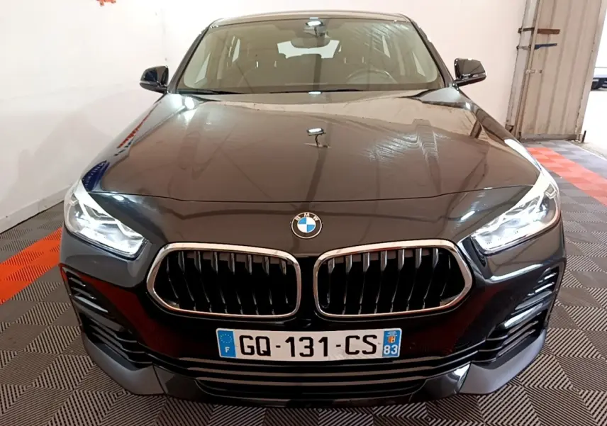 Vue avant rapprochée d’un BMW X2 sDrive18i Lounge noir avec calandre double haricot et phares LED allumés.