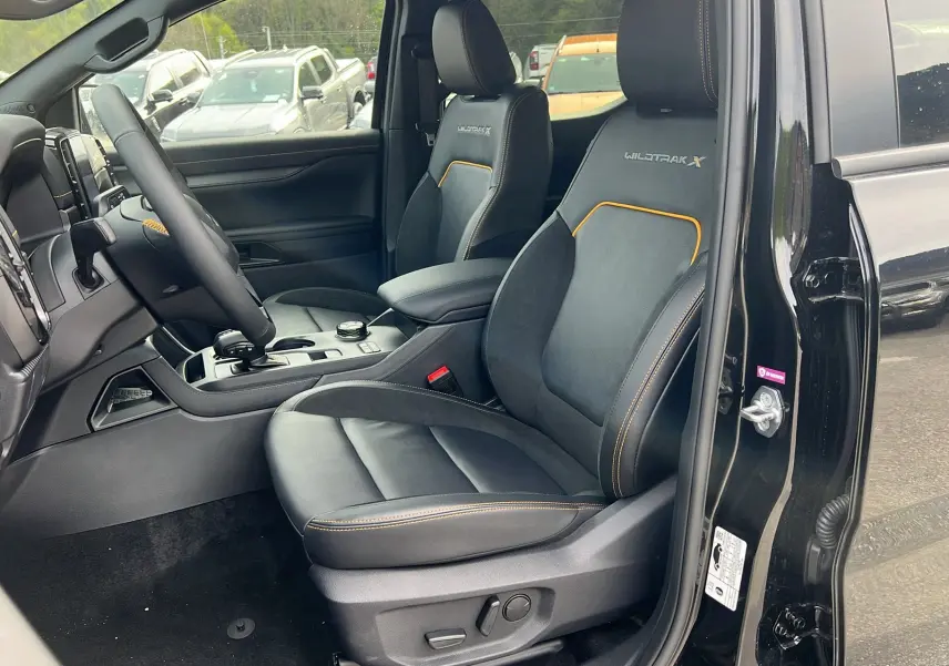 Vue intérieure côté conducteur du Ford Ranger Wildtrak X 2026 noir agate, sièges en cuir avec surpiqûres orange et logo Wildtrak X brodé.