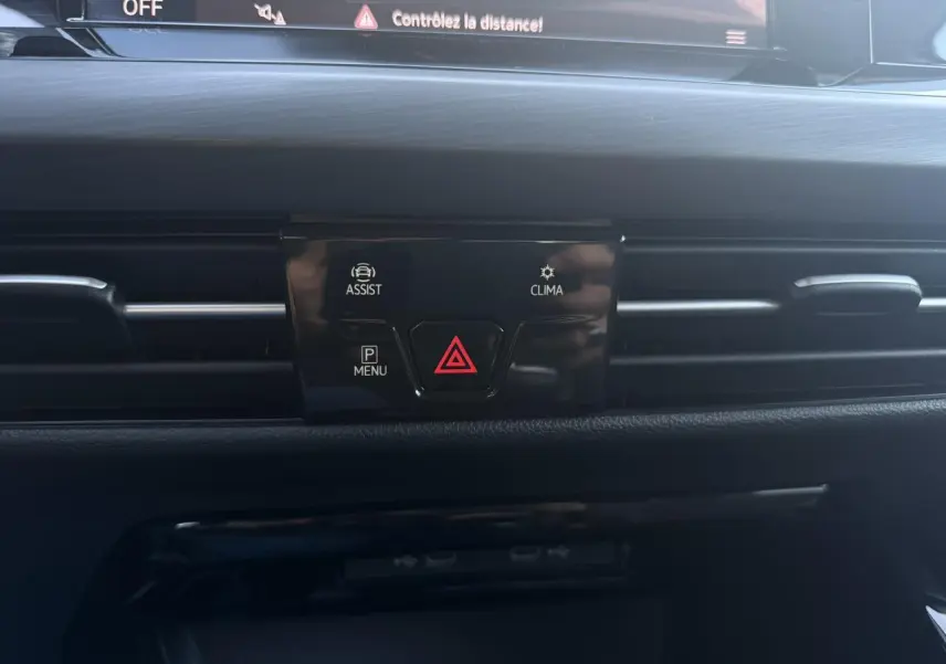 Gros plan sur la console centrale noire de la Volkswagen Golf VIII 2024, avec boutons d'assistance et climatisation visibles.