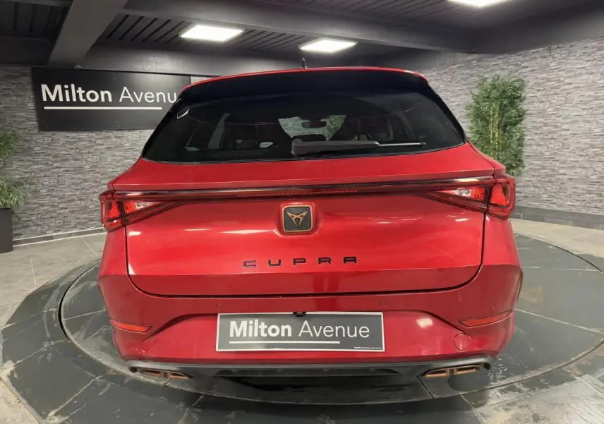 Vue arrière d'une CUPRA Leon Sportstourer rouge Désir avec feux LED et logo CUPRA sur fond noir.