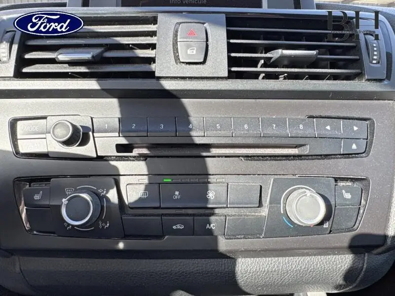 Détail de la console centrale noire d'une BMW Série 1 114i 2013 avec commandes de climatisation et radio.