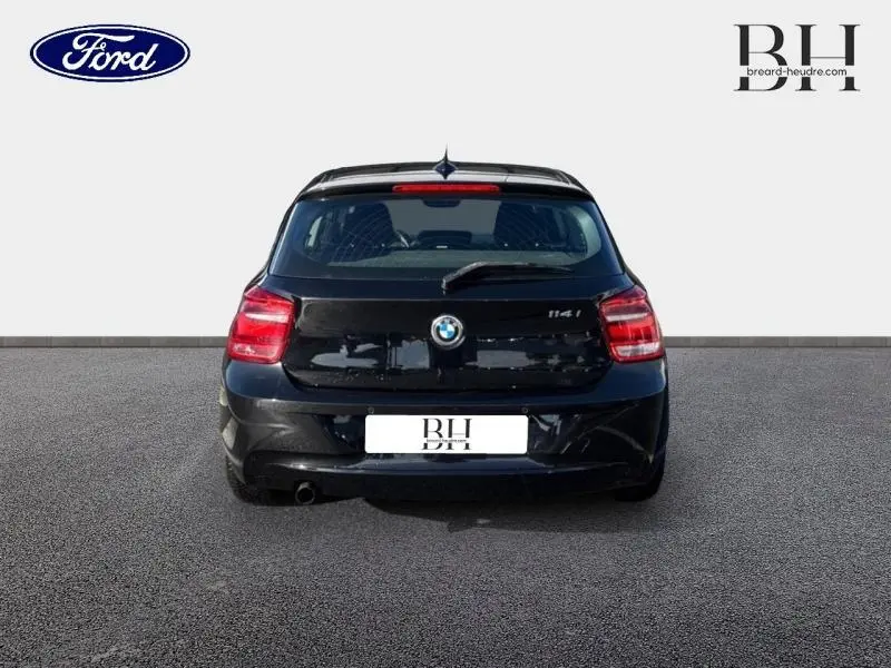 Vue arrière d'une BMW Série 1 114i noire de 2013 avec feux arrière rouges et becquet sur le hayon.