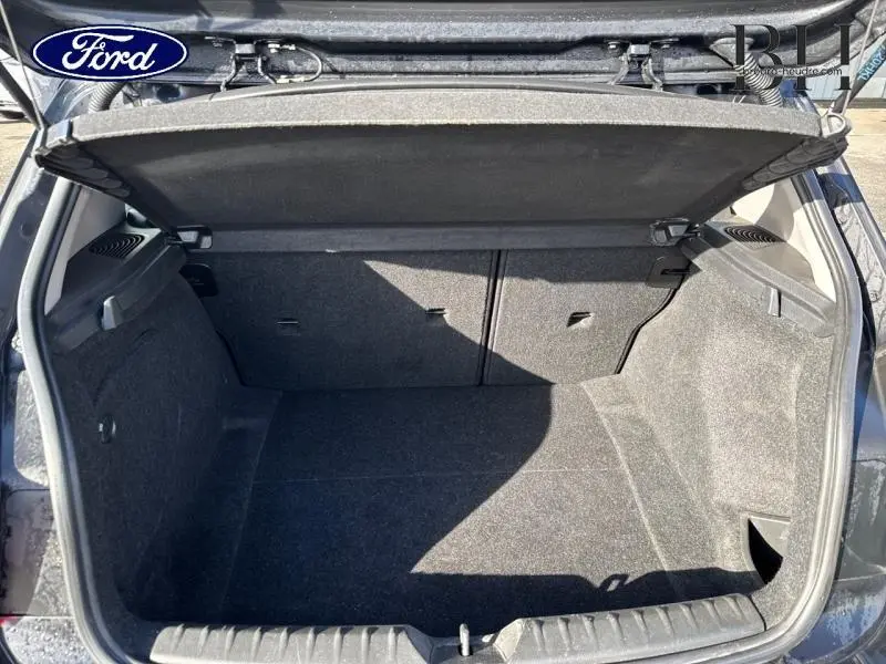 Coffre ouvert vu de l'arrière d'une BMW Série 1 noire, montrant l'espace de chargement et la tablette cache-bagages.