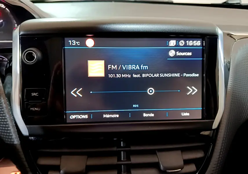 Écran tactile central allumé du tableau de bord d’un Peugeot 2008 gris foncé, affichant une radio FM.