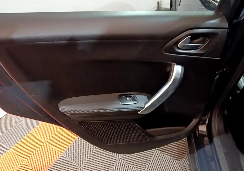 Vue rapprochée de la porte avant droite noire du Peugeot 2008 gris foncé avec poignée argentée et commande de vitre.