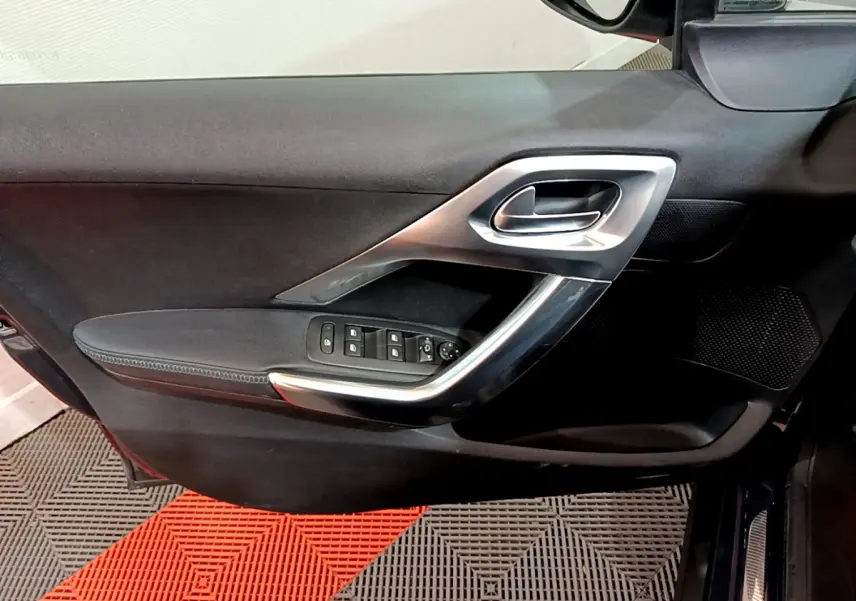 Vue intérieure côté gauche de la porte avant d'une Peugeot 2008 gris foncé avec commandes de vitres et poignée argentée.
