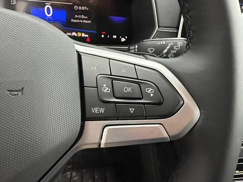 Gros plan sur les commandes au volant côté droit du Volkswagen T-Cross 2025 gris Ascot, avec affichage numérique en arrière-plan.