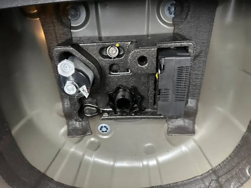 Détail du compartiment de rangement sous le plancher de coffre du Volkswagen T-Cross 2025 Gris Ascot, montrant les fixations et outils.