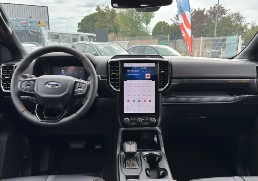 Vue intérieure frontale du Ford Ranger 2025 Wildtrak Plus, tableau de bord noir avec écran tactile vertical et volant cuir multifonctions.