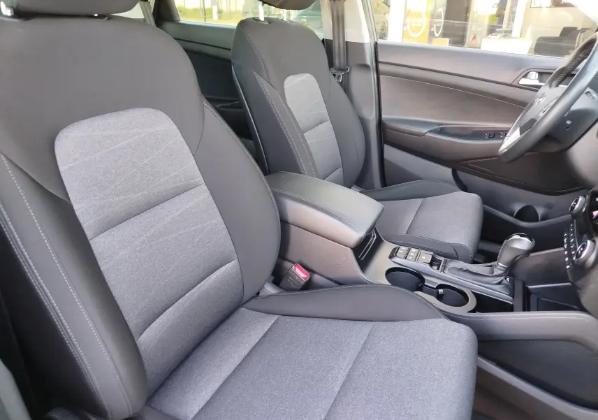 Vue intérieure côté conducteur du Hyundai Tucson 2019, sièges tissu gris et console centrale avec levier de vitesse automatique.