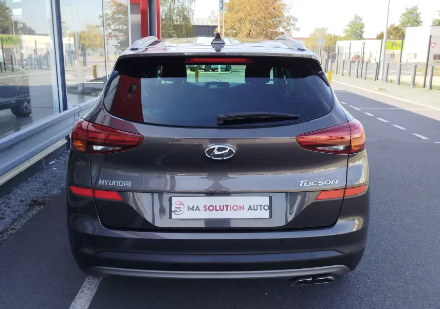 Vue arrière d'un Hyundai Tucson gris Micron garé, avec feux arrière allongés et double sortie d'échappement visible.
