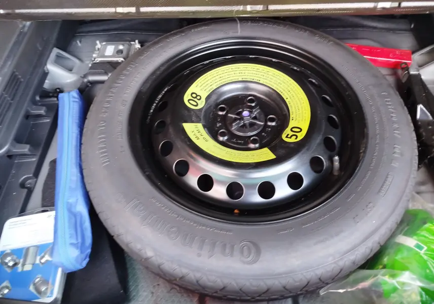 Vue rapprochée de la roue de secours noire avec étiquette jaune dans le coffre d'un Hyundai Tucson gris Micron.