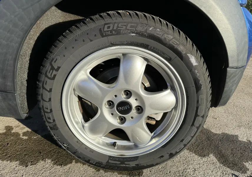 Gros plan sur la roue avant droite d'une MINI Cooper bleu, avec jante argentée et pneu Cooper Discoverer.