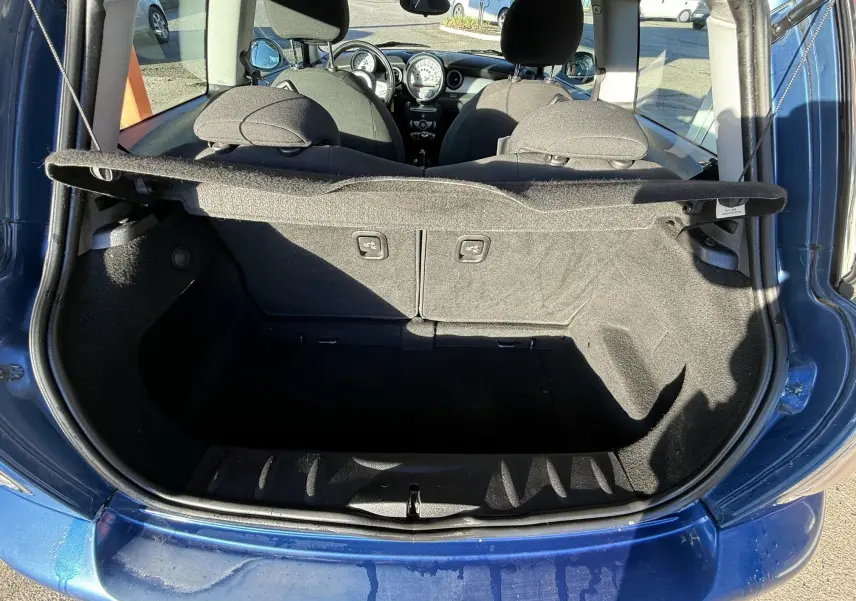 Coffre ouvert vu de l'arrière d'une MINI Cooper bleu, montrant l'intérieur noir et les sièges avant.