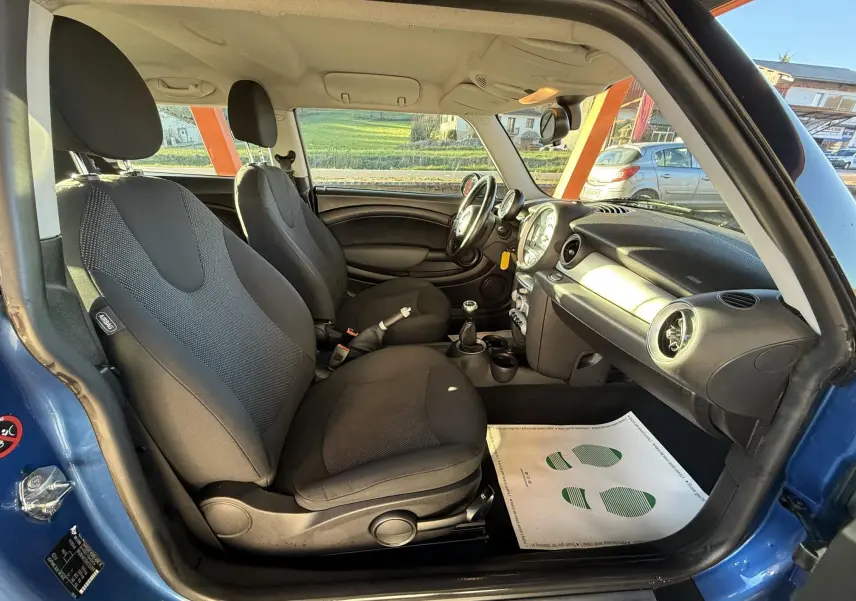 Vue intérieure côté conducteur de la MINI Cooper 1.6 bleu de 2007 avec sièges tissu gris et volant cuir.