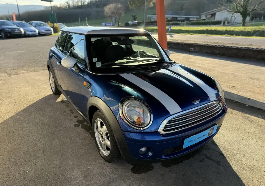 Vue 3/4 avant d'une MINI Cooper bleu foncé avec toit blanc et bandes blanches sur le capot, stationnée en extérieur.