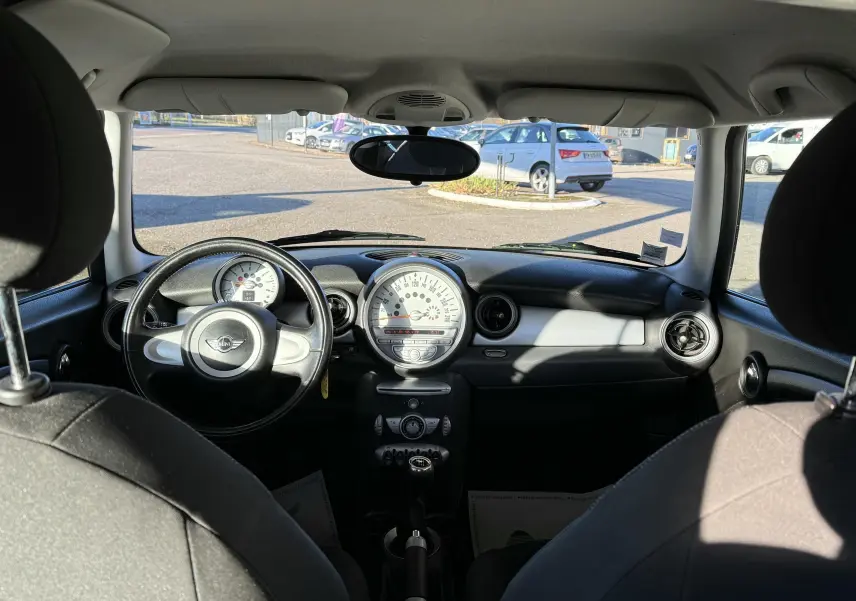 Vue intérieure avant de la MINI Cooper 2007 avec tableau de bord noir et gris, volant cuir et compteur central rond.