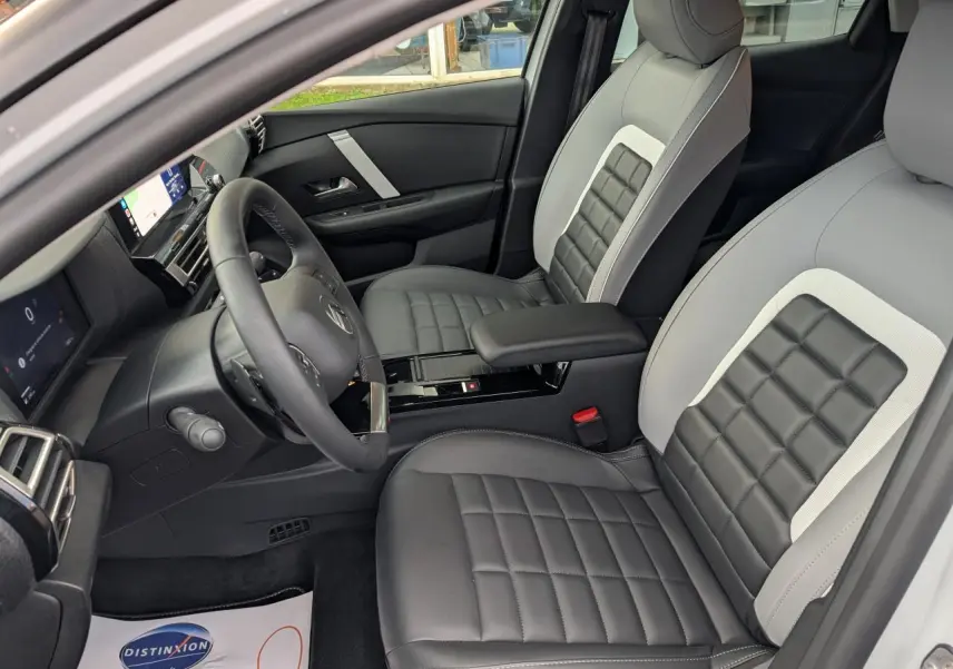 Intérieur de la Citroën C4 2025 vu côté conducteur, sièges gris et noirs avec console centrale noire brillante.