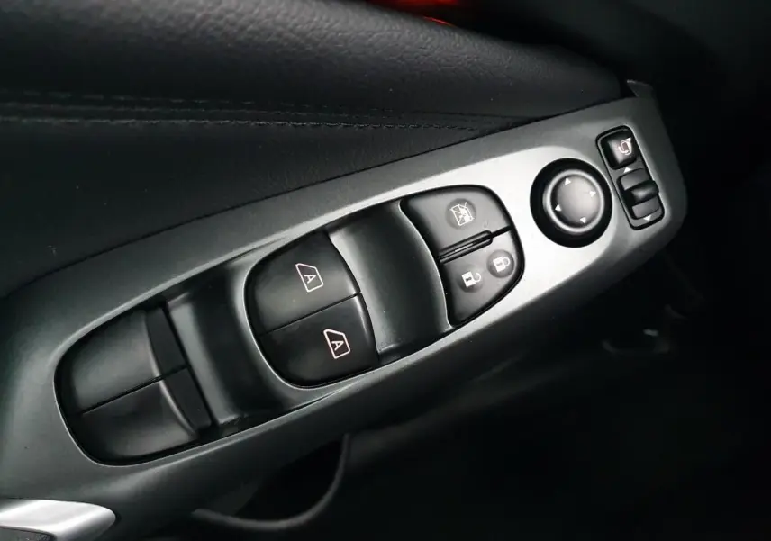 Gros plan sur les commandes de lève-vitres et rétroviseurs côté gauche intérieur du Nissan Juke noir 2025.