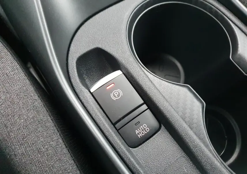 Gros plan sur le frein à main électrique et porte-gobelets noirs dans l'habitacle du Nissan Juke 2025.