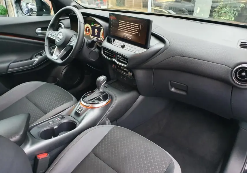 Intérieur avant droit du Nissan Juke 2025 noir, avec console centrale, écran tactile et volant multifonctions.
