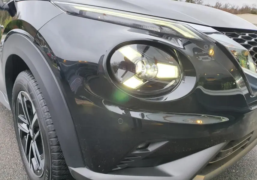 Gros plan sur l'avant droit noir métallisé du Nissan Juke 2025 avec phare allumé et jante alliage 17 pouces.