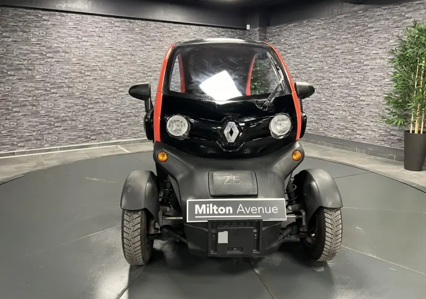 Vue frontale d'une Renault Twizy Intens 2019 orange avec logo Renault et phares ronds dans un showroom.