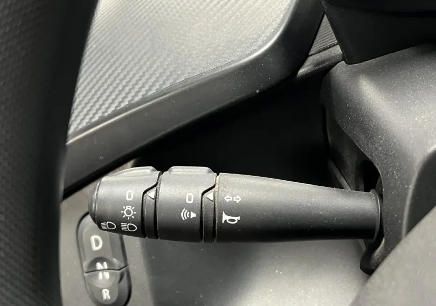 Gros plan sur la manette de clignotants noire côté gauche du tableau de bord d'une Renault Twizy orange.