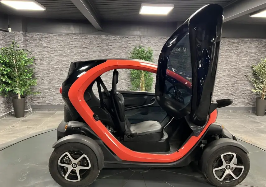Profil droit d'une Renault Twizy orange 2019 avec porte élytre ouverte, montrant l'intérieur compact et les sièges noirs.