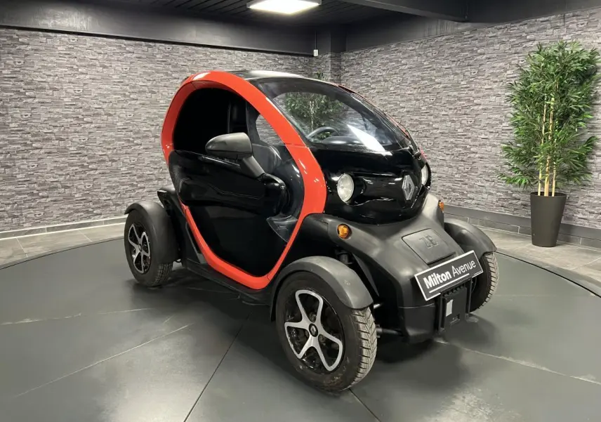 Vue 3/4 avant droite de la Renault Twizy Intens 2019 orange et noire, petite voiture électrique compacte en intérieur showroom.