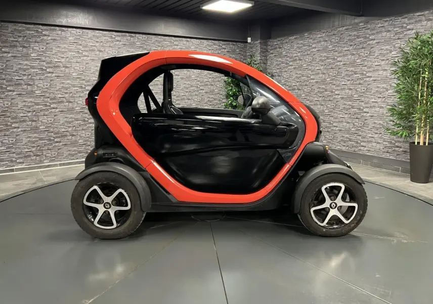 Profil droit de la Renault Twizy Intens 2019 orange et noir, petite voiture électrique compacte en intérieur showroom.