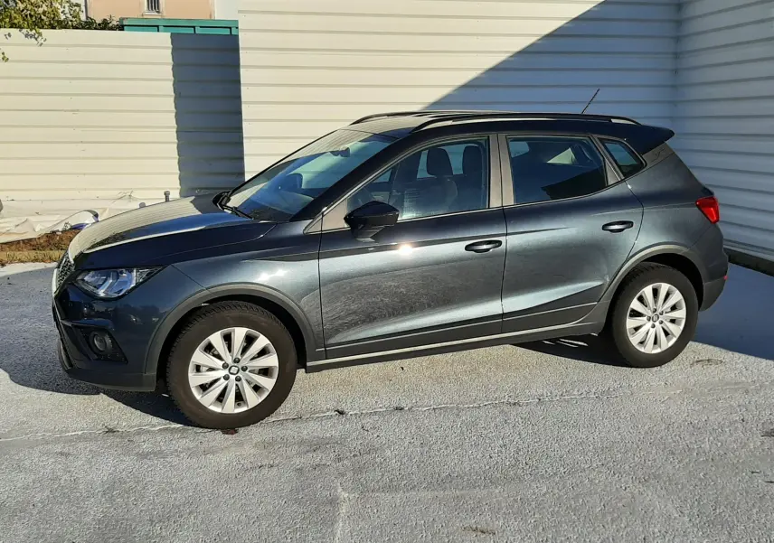 SEAT Arona gris magnetic avec toit noir, vue de profil côté gauche sur fond urbain lumineux.