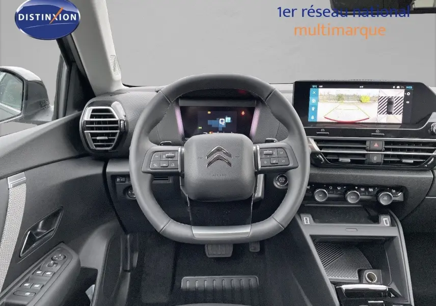 Vue intérieure frontale du poste de conduite de la Citroën C4 gris platinium, avec volant multifonction et écran tactile affichant la caméra de recul.