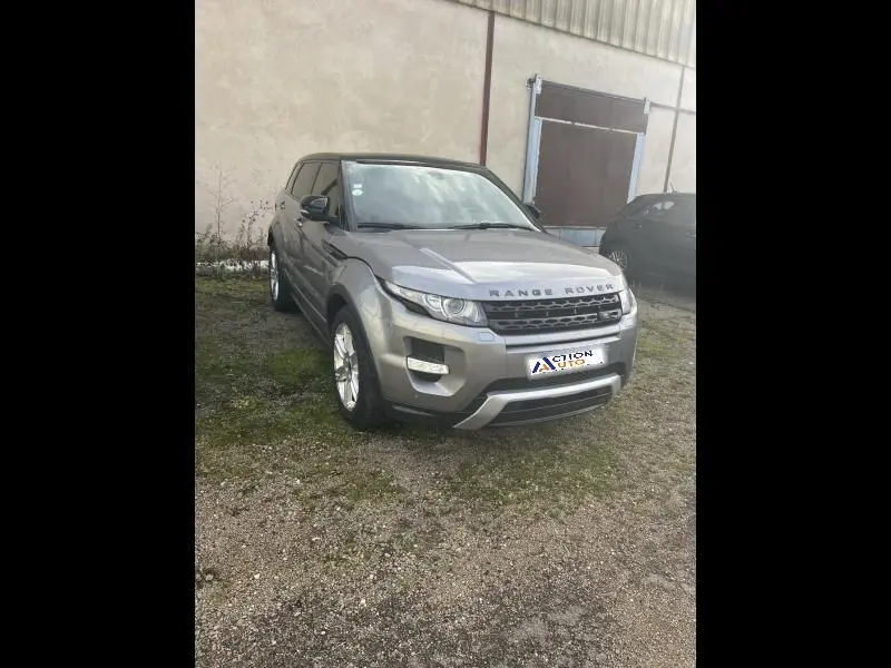 Range Rover Evoque gris Orkney vu en 3/4 avant droit, stationné devant un bâtiment industriel.