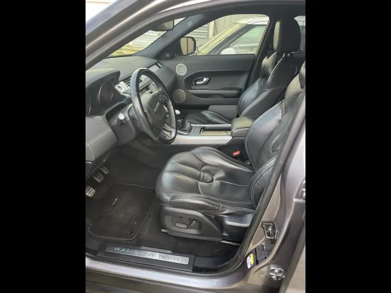 Vue intérieure côté conducteur du Range Rover Evoque gris Orkney de 2013, avec sellerie cuir noire et tableau de bord moderne.